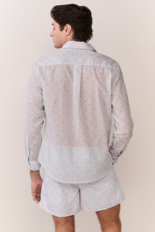 Person wearing a light-colored patterned shirt and shorts set against a plain background