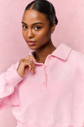 Woman wearing a pink polo long sleeve shirt against a pink background