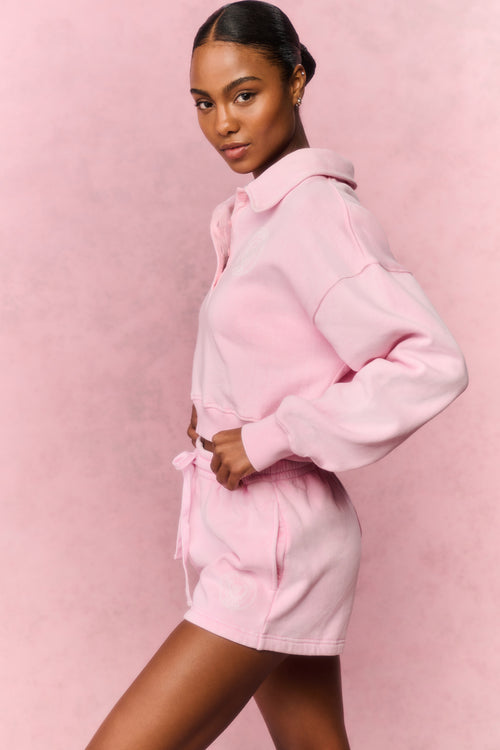 Woman wearing a pink hoodie and short set against a pink background