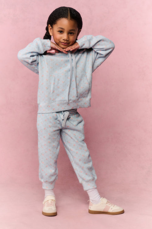 Young girl wearing a light blue tracksuit against a pink background