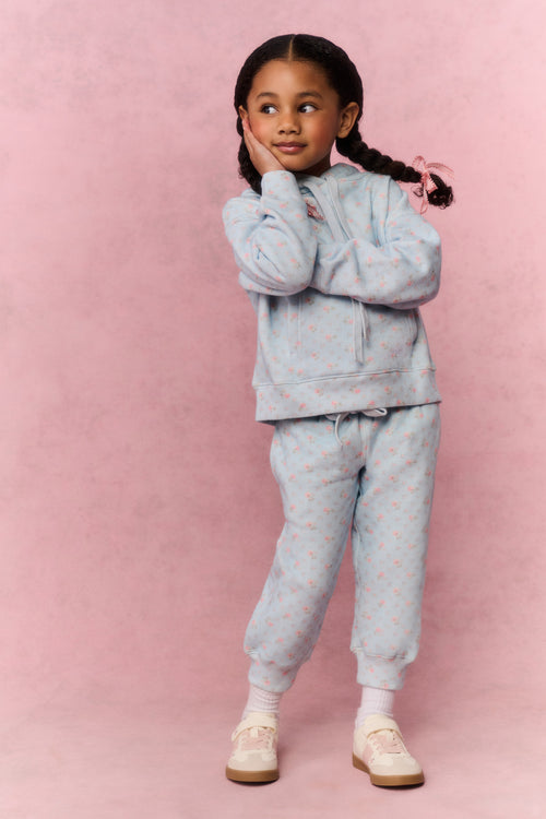 Young girl wearing a light blue tracksuit against a pink background