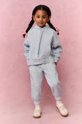 Young girl wearing a light blue tracksuit against a pink background