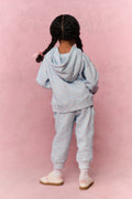Child wearing a light blue tracksuit against a pink background