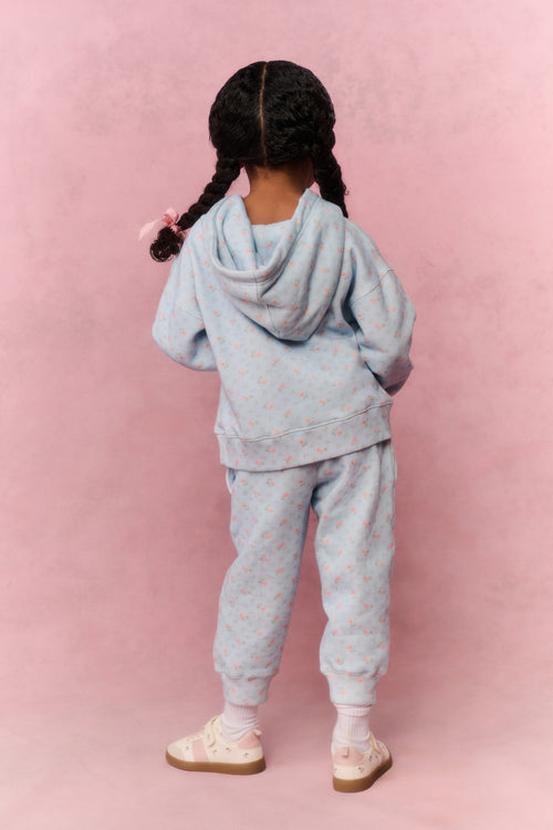 Child wearing a light blue tracksuit against a pink background