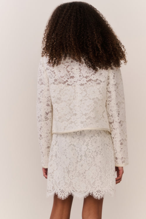 Tween wearing a white lace jacket and mini dress outfit on a plain background