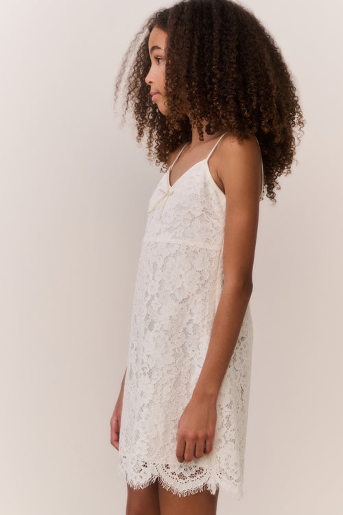 Girl wearing a white lace dress against a plain background