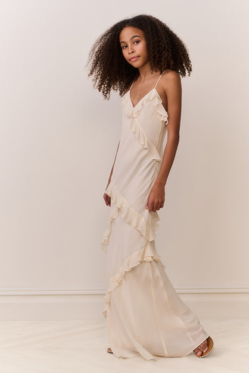 Tween girl wearing a flowing white sleeveless dress with ruffles on a plain background