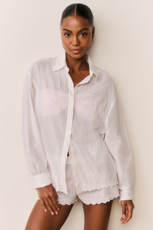Woman wearing a white linen shirt and shorts on a plain background