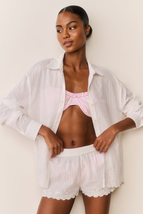 Woman wearing a white button down over a pink bikini with matching shorts a plain background
