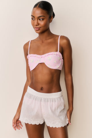 Woman wearing a white button down over a pink bikini with matching shorts a plain background