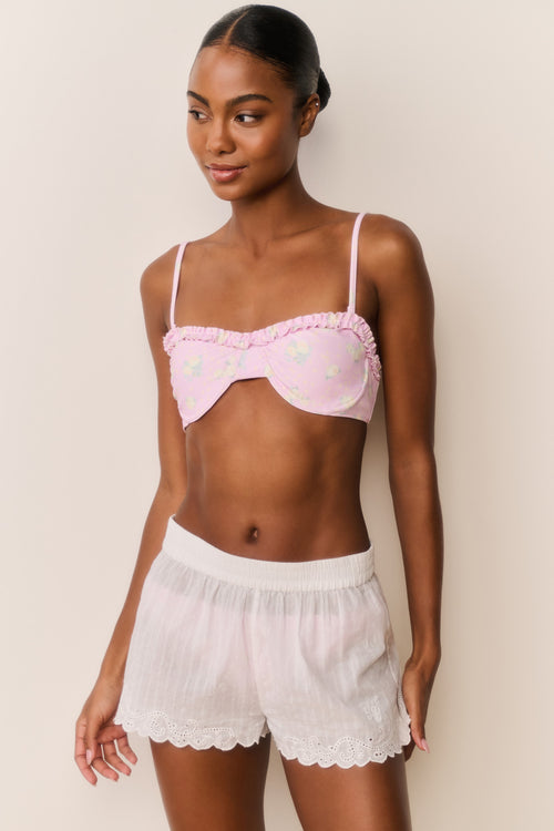 Woman wearing a white button down over a pink bikini with matching shorts a plain background