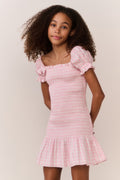 Girl wearing a pink checkered dress with a plain background