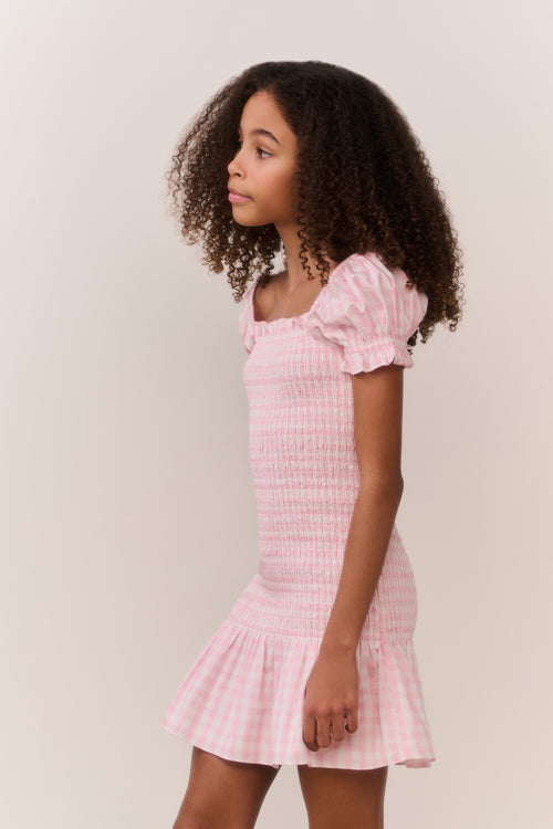 Girl wearing a pink checkered dress with a plain background