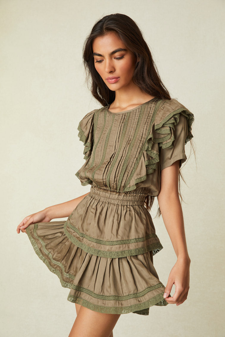 Model wearing green mini dress with ruffled skirt and shoulders and lace detail