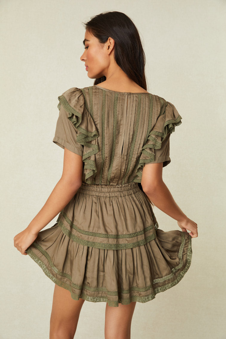 Model wearing green mini dress with ruffled skirt and shoulders and lace detail