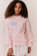 Girl wearing a pink american flag sweatshirt and white lace skirt on a plain background