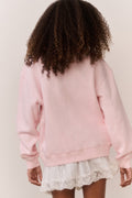 Girl wearing a pink american flag sweatshirt and white lace skirt on a plain background