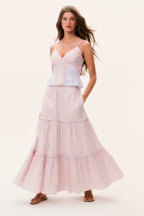 Woman wearing a light pink tiered maxi skirt and matching camisole top on a white background