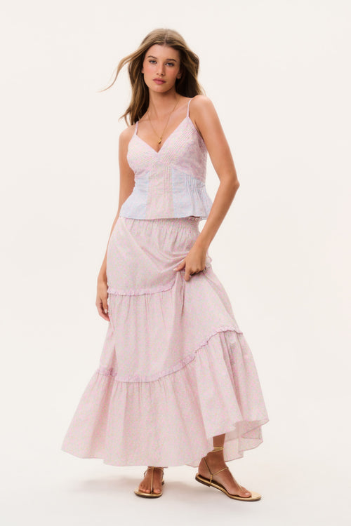 Woman wearing a light pink tiered maxi skirt and matching camisole top on a white background