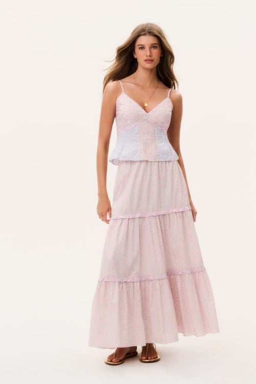 Woman wearing a light pink tiered maxi skirt and matching camisole top on a white background
