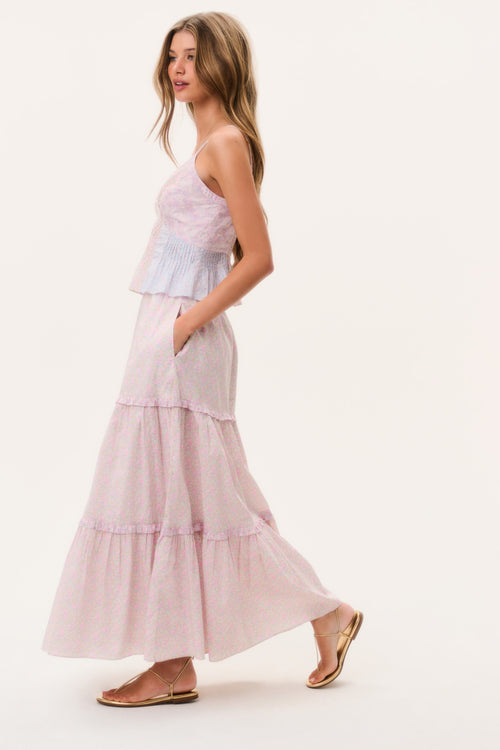 Woman wearing a light pink tiered maxi skirt and matching camisole top on a white background