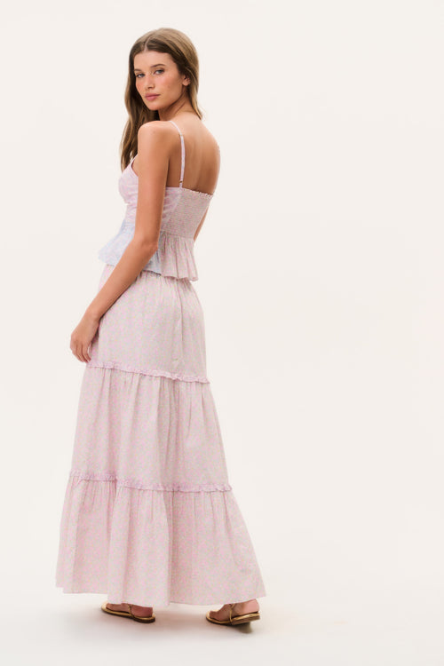 Woman wearing a light pink tiered maxi skirt and matching camisole top on a white background