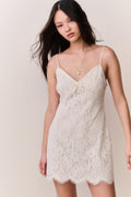 Woman wearing a white lace slip dress against a plain background