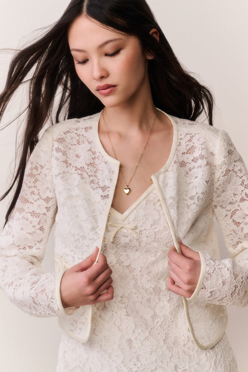 Woman wearing a white lace outfit against a plain background