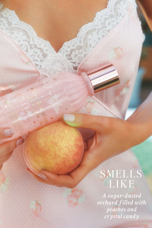 Person holding a peach with a perfume bottle, wearing a lace dress.