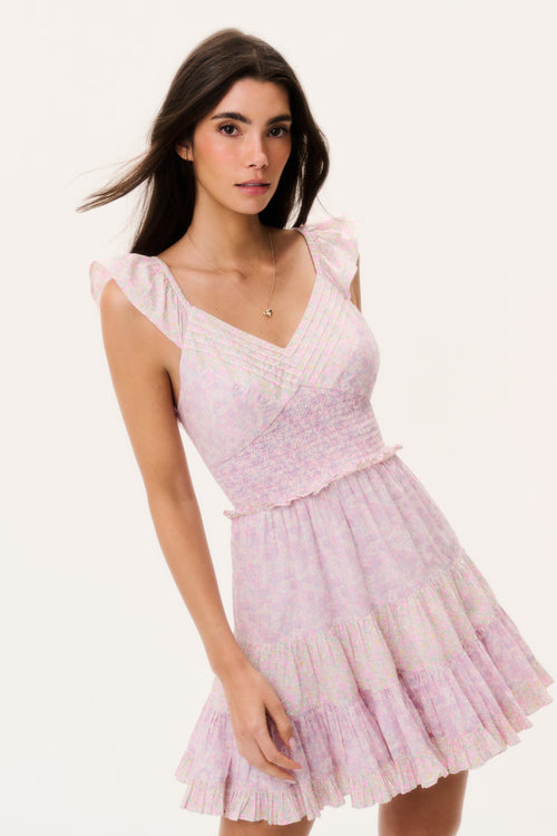 Woman wearing a pink mini dress with ruffled cap sleeves on a white background