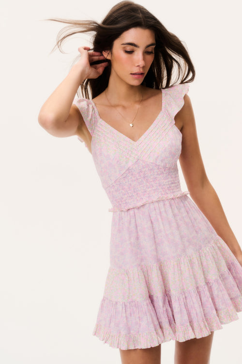 Woman wearing a pink mini dress with ruffled cap sleeves on a white background