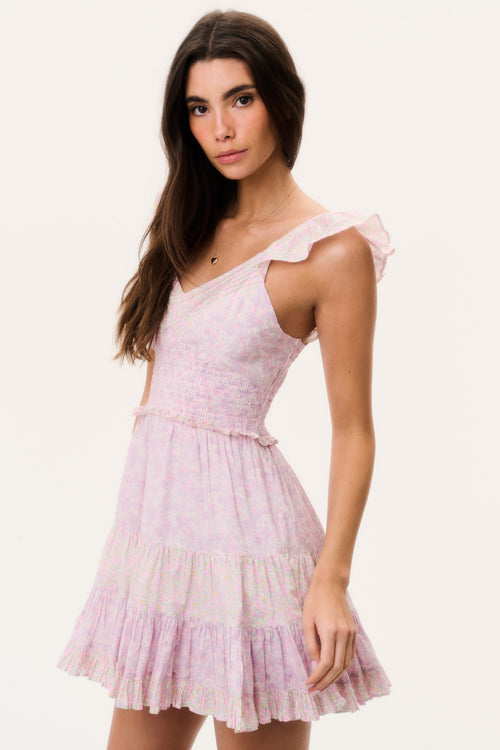 Woman wearing a pink mini dress with ruffled cap sleeves and open back on a white background