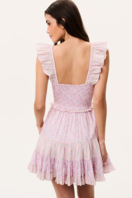 Woman wearing a pink mini dress with ruffled cap sleeves and open back on a white background