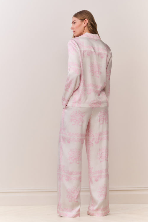 Person wearing a pink and white patterned button down and matching pants outfit on a plain background