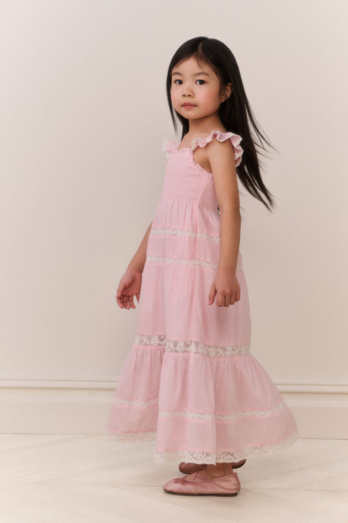 Young girl wearing a pink dress with ruffled straps and lace details on a white background