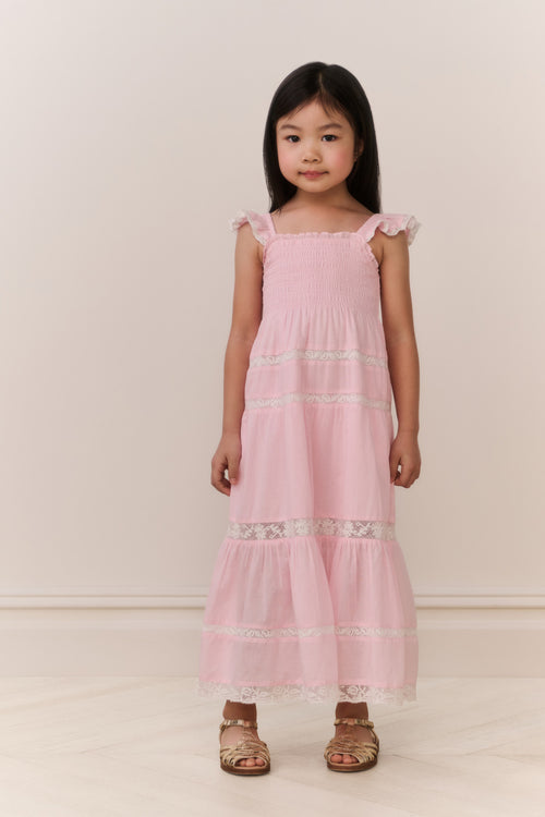 Young girl wearing a pink dress with lace details against a white background