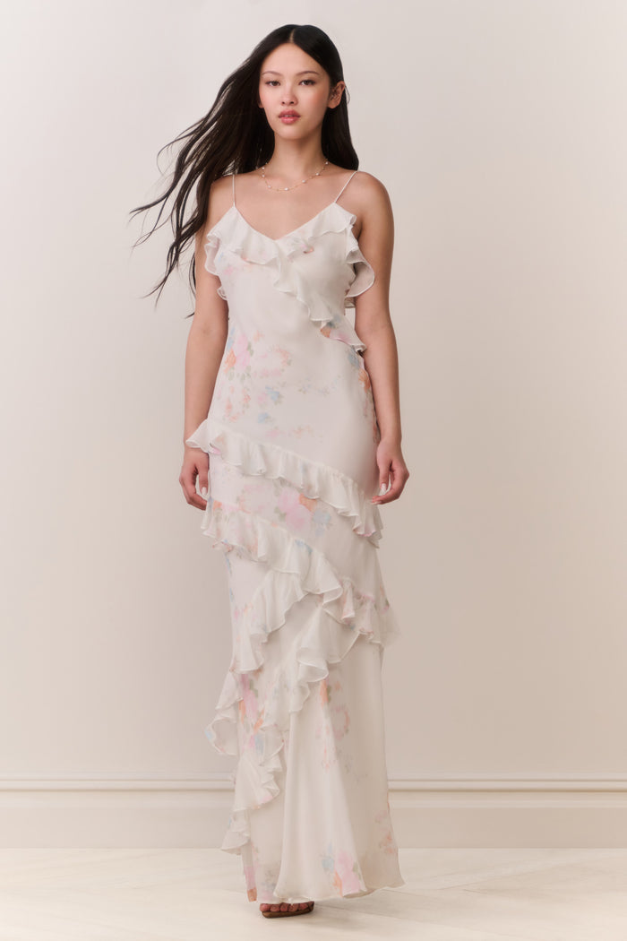 Woman wearing a white floral ruffle tiered sleeveless maxi dress against a plain background