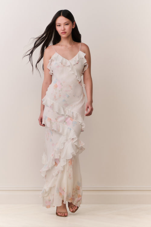 Woman wearing a white floral ruffle tiered sleeveless dress against a plain background