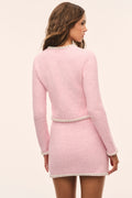 A woman shown from the back wearing a light pink textured tweed mini dress with white trim details, set against a plain cream background.