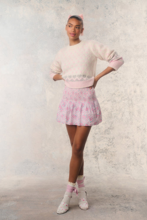 Person wearing a light pink sweater and skirt with a white background