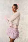 Woman wearing a light pink sweater and matching skirt with a subtle pattern on a light background