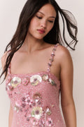 Woman wearing a pink dress with floral embellishments on a plain background