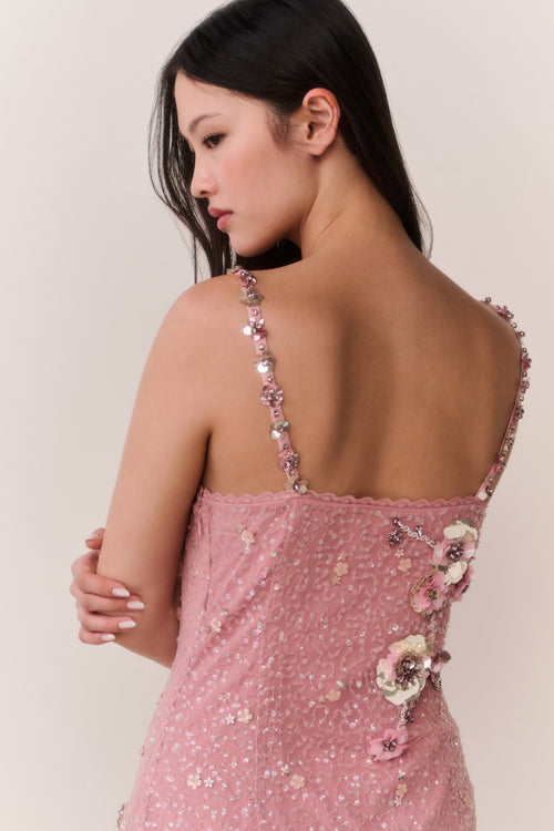 Woman wearing a pink dress with floral embellishments against a plain background