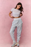 Woman wearing a light blue floral t-shirt and sweatpants against a pink background