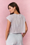 Woman wearing a light blue floral top and pants against a pink background