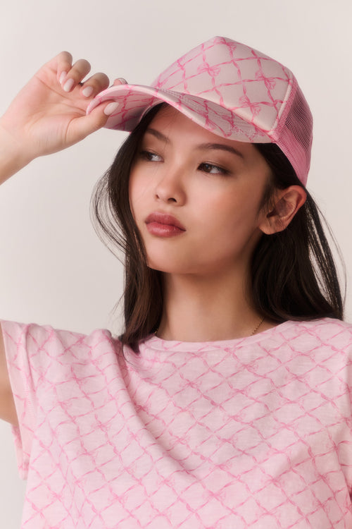 Woman wearing a pink bow print cap and matching tee against a white background