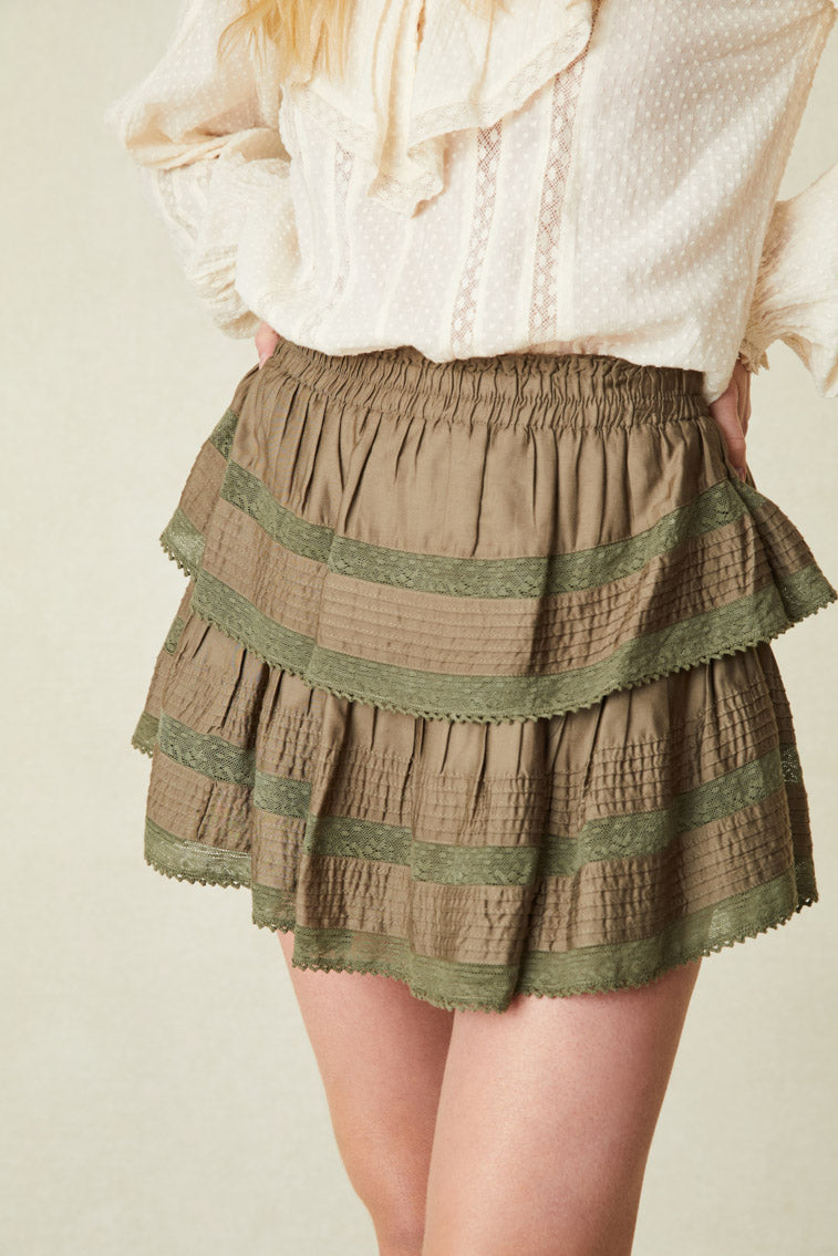Model wearing green ruffle mini skirt with lace hem on the ruffles.