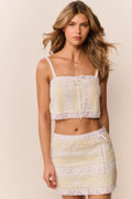 Woman wearing a white and yellow lace cropped top with matching skirt against a beige background