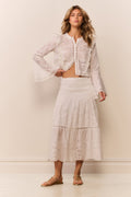 Woman wearing a white lace eyelet maxi skirt and matching long sleeve blouse against a plain background