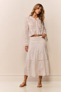 Woman wearing a white lace eyelet maxi skirt and matching long sleeve blouse against a plain background